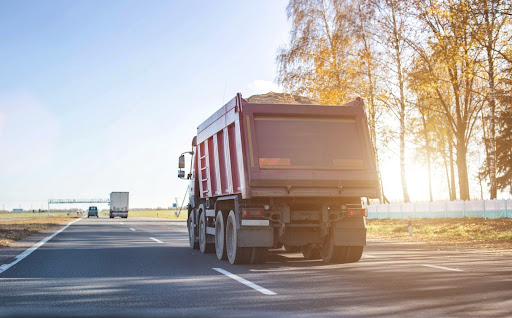 Dump truck carrying uncovered load of sand down divided highway; risk factors for dump truck accidents.