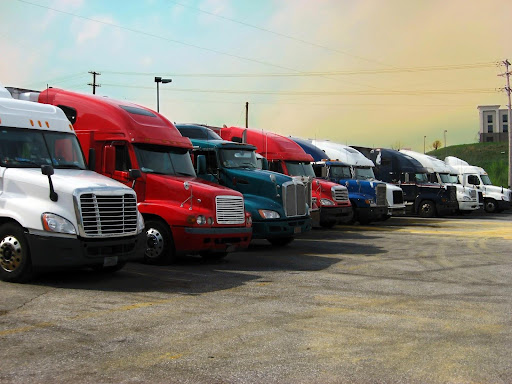 A row of semi-trucks in various colors at a truck stop. Trucking laws exist for many reasons, including protecting other drivers.