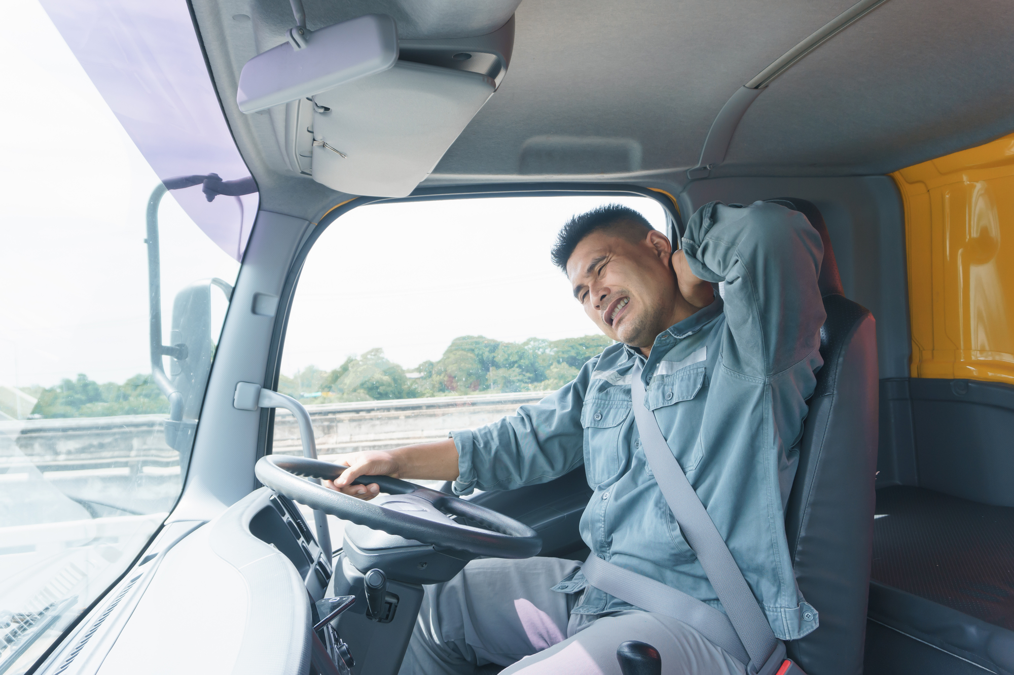 A tired truck driver yawning in his truck, thinking about hours of service regulations.