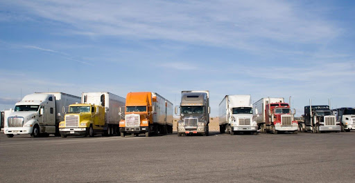 A row of semi-trucks in a parking lot. The Department of Transportation regulations for truck drivers can impact both truck drivers and trucking companies.